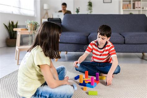 Two Kids Playing Together on the Floor while Their Father Working with ...