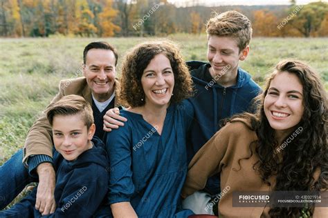 A happy family of five sitting together in a field — father, memories ...